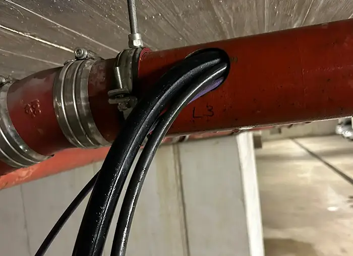 Schwarze Kabel ragen aus einem roten Rohr mit "L3" und "23" in einer Tiefgarage.